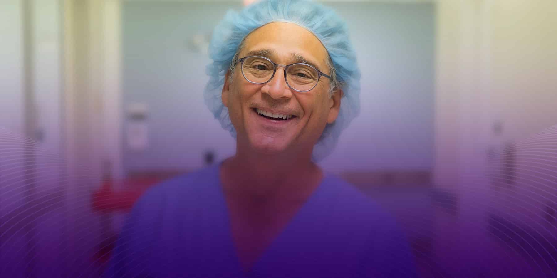 NYU male doctor smiling at the camera and standing in the hospital hall with his surgical cap on