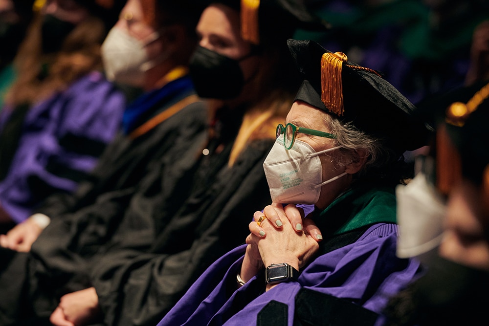 People sitting in their cap and gown at a NYU graduation ceremony