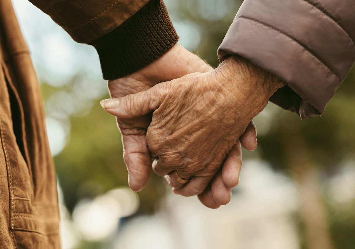 Close up of elderly couple holding hands and walking outdoors. Rear view of man and woman holding hands of each other while walking outdoors.