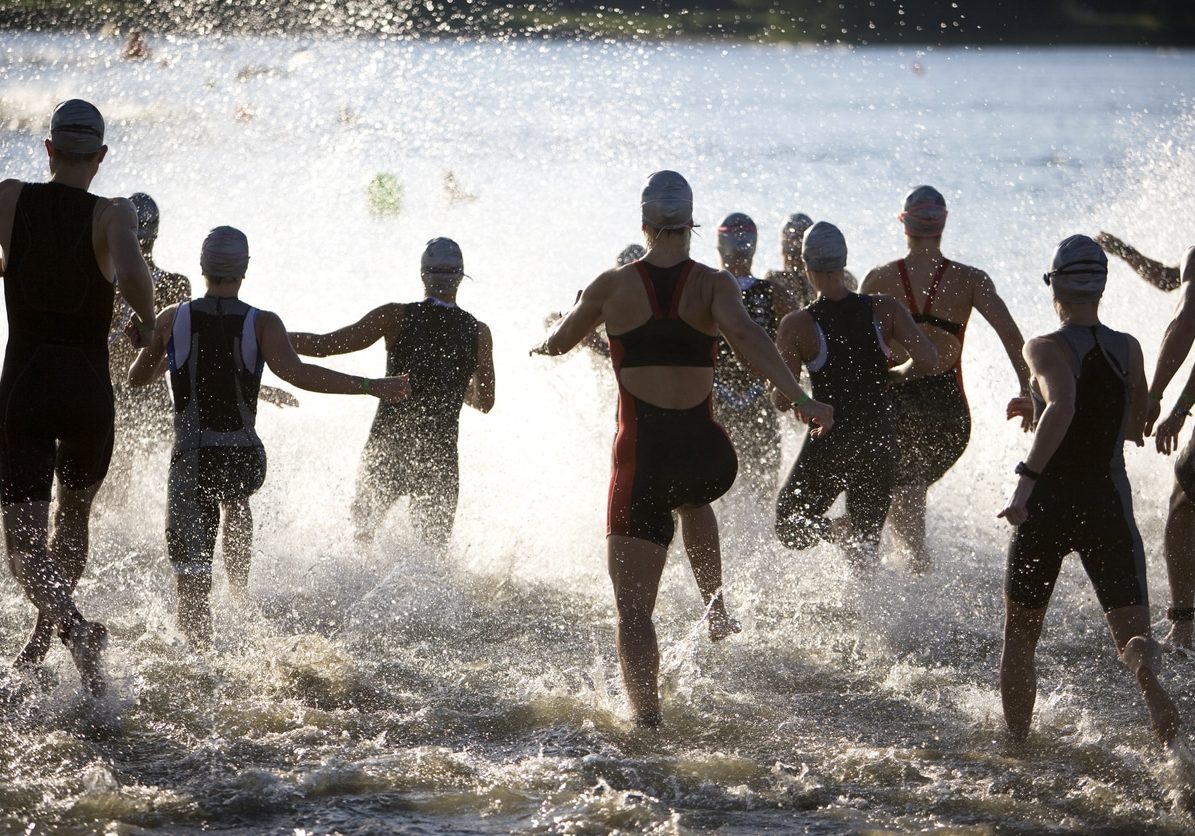 Triathletes At Start Of Triathlon Running Into The Water.