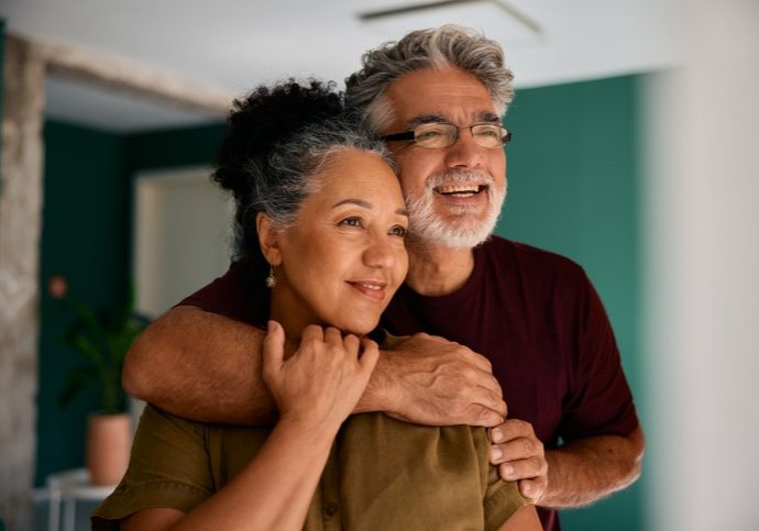 Happy Senior Couple Embracing And Looking Away At Home