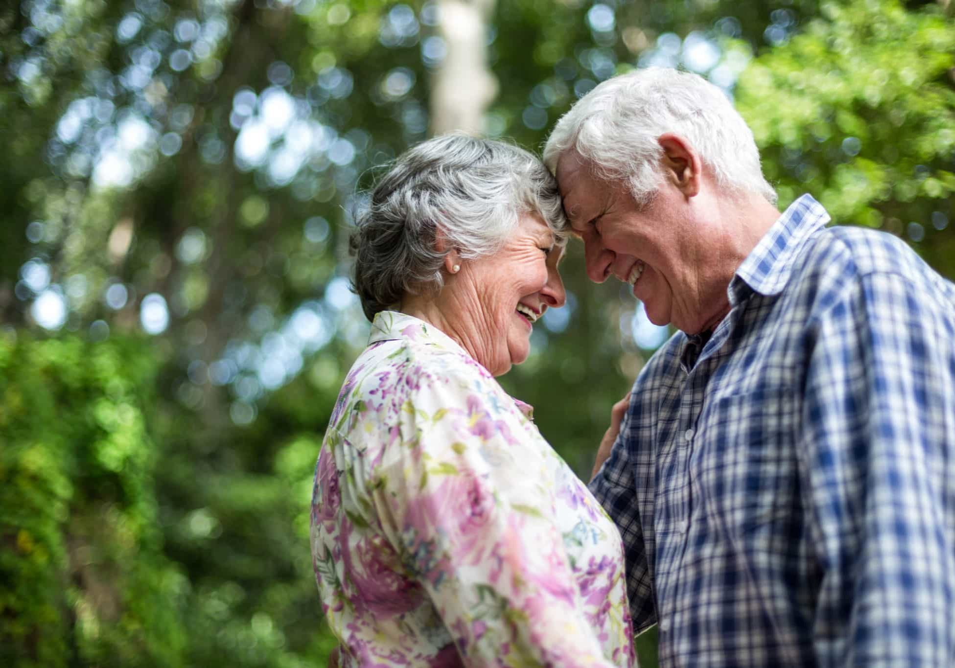Romantic senior couple touching head against trees in back yard